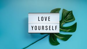 A light box sign reading 'Love yourself', beside a monstera leaf