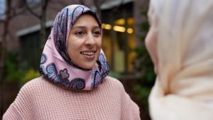 A young woman in a patterned hijab smiling during a conversation