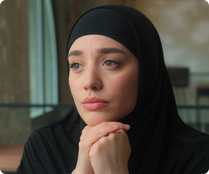 A young woman in a black hijab resting her chin on her hands, looking thoughtful