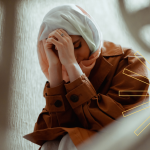 A young woman in a hijab sitting with her head in her hands