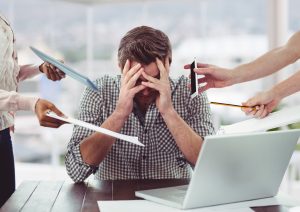 A man sitting with his hands over his face while colleagues hand him paperwork