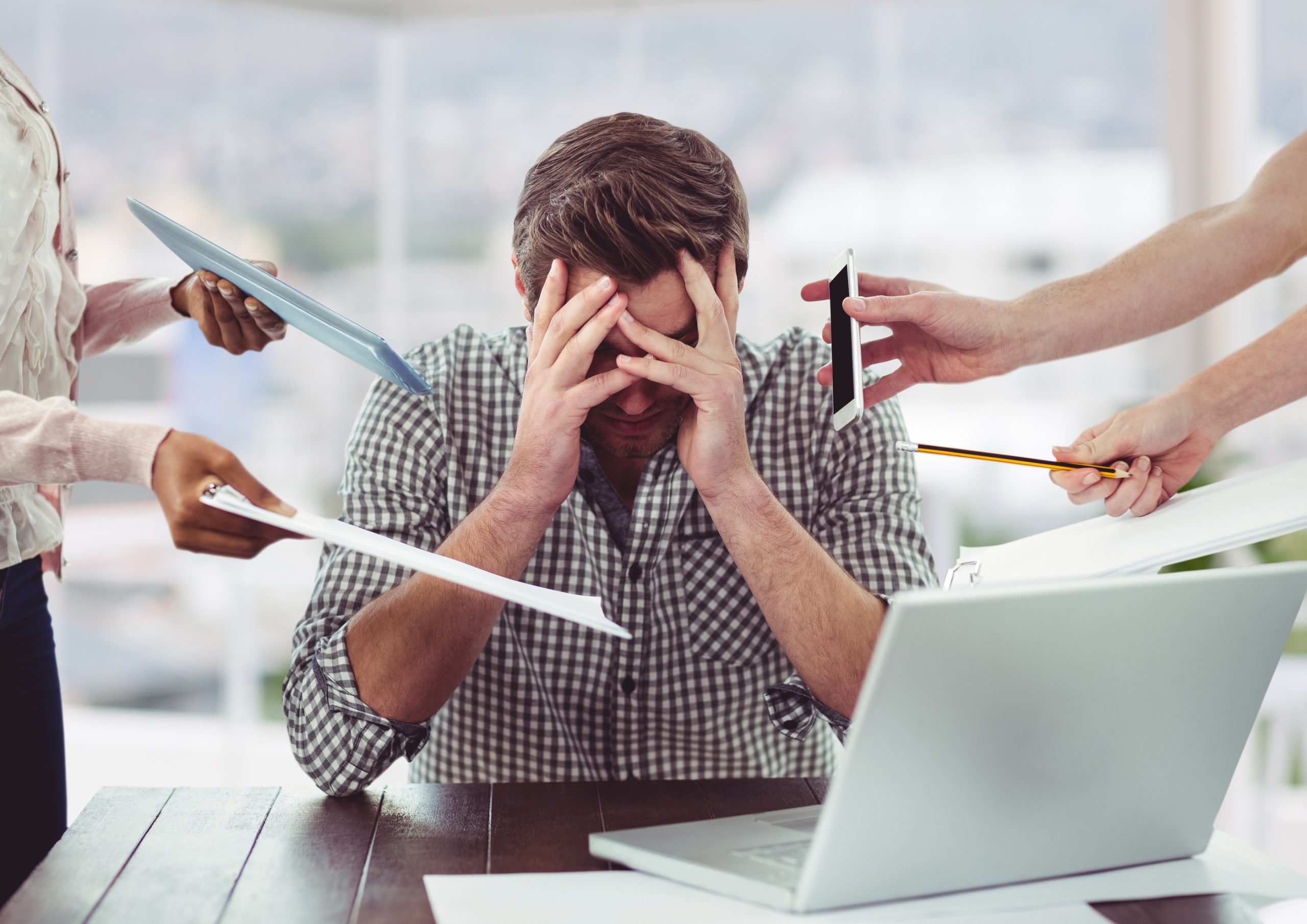 A man sitting with his hands over his face while colleagues hand him paperwork