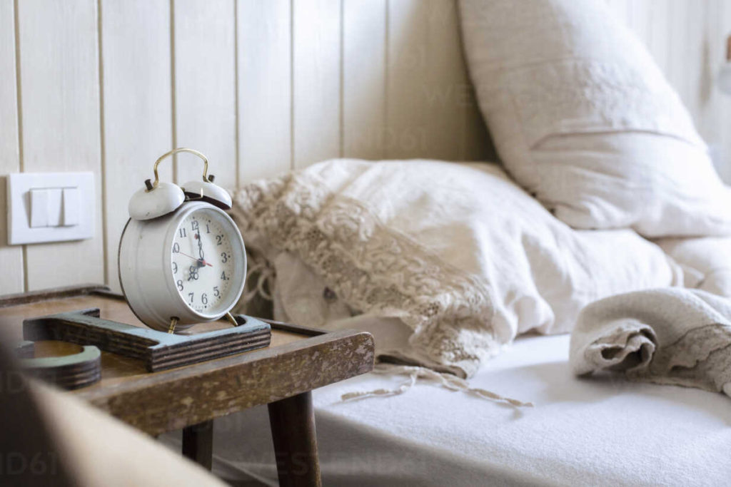 An alarm clock on a bedside table next to a bed