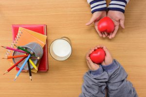 Children's hands holding red hearts above a desk with pencils and books