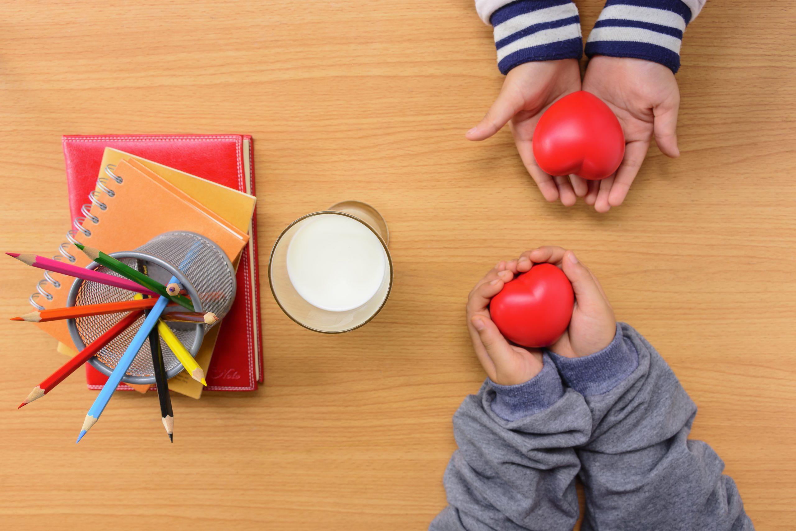 Children's hands holding red hearts above a desk with pencils and books