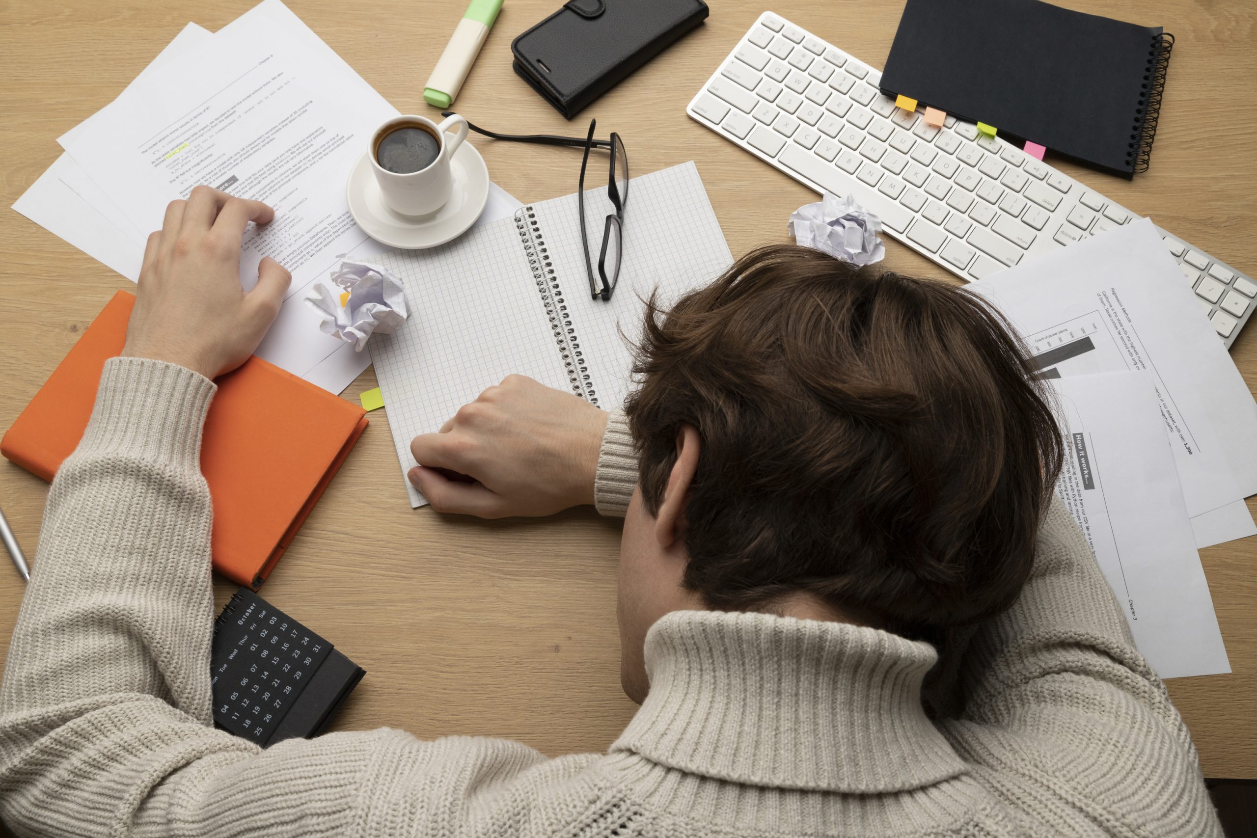 A student at a desk covered in papers, holding their head