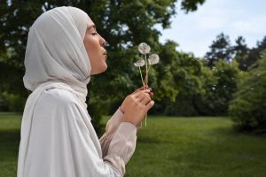 A young woman in a hijab in a park, holding dandelion seed heads