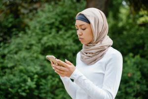 A young woman in a hijab outdoors, using a phone