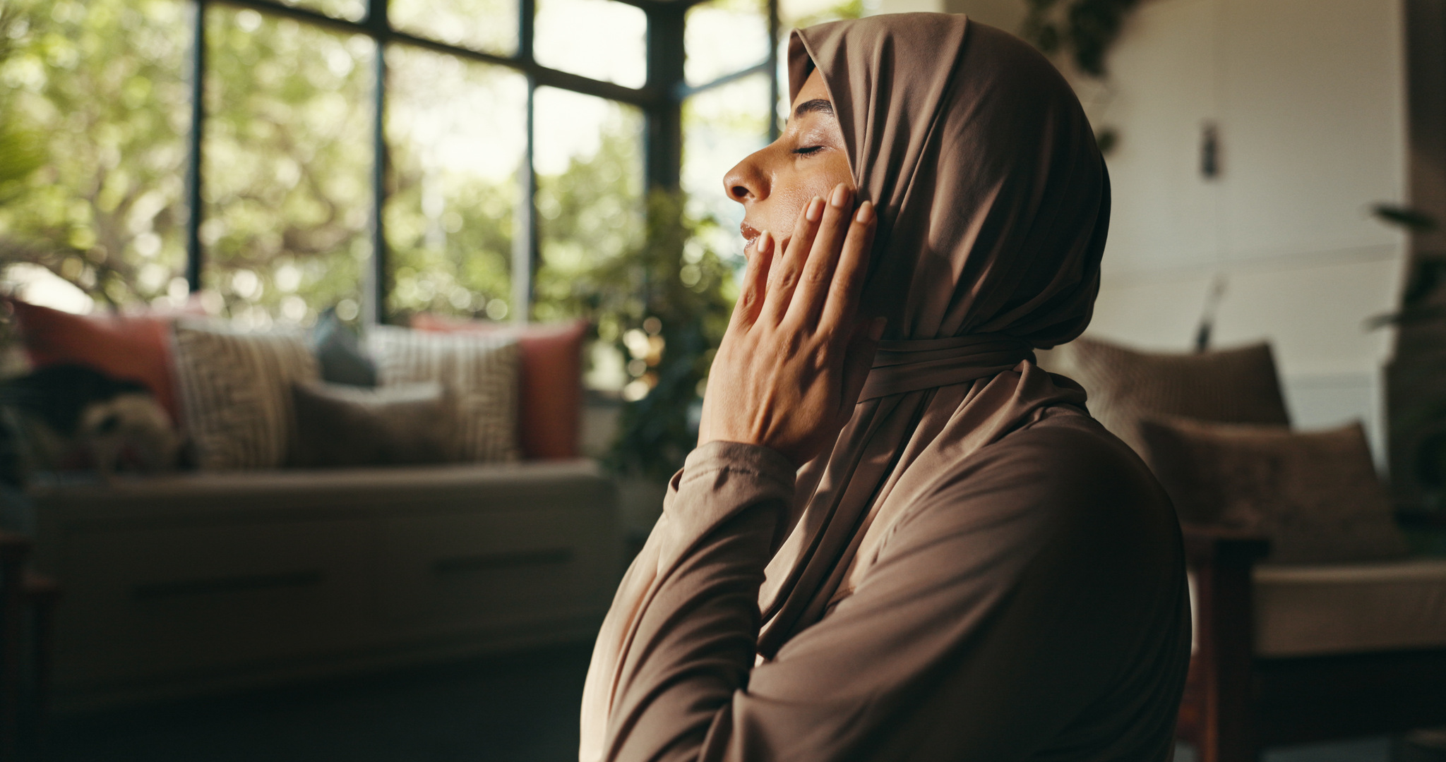 A woman in a hijab praying with her hands raised