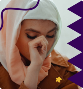 A young woman in a hijab pinching the bridge of her nose, looking tired