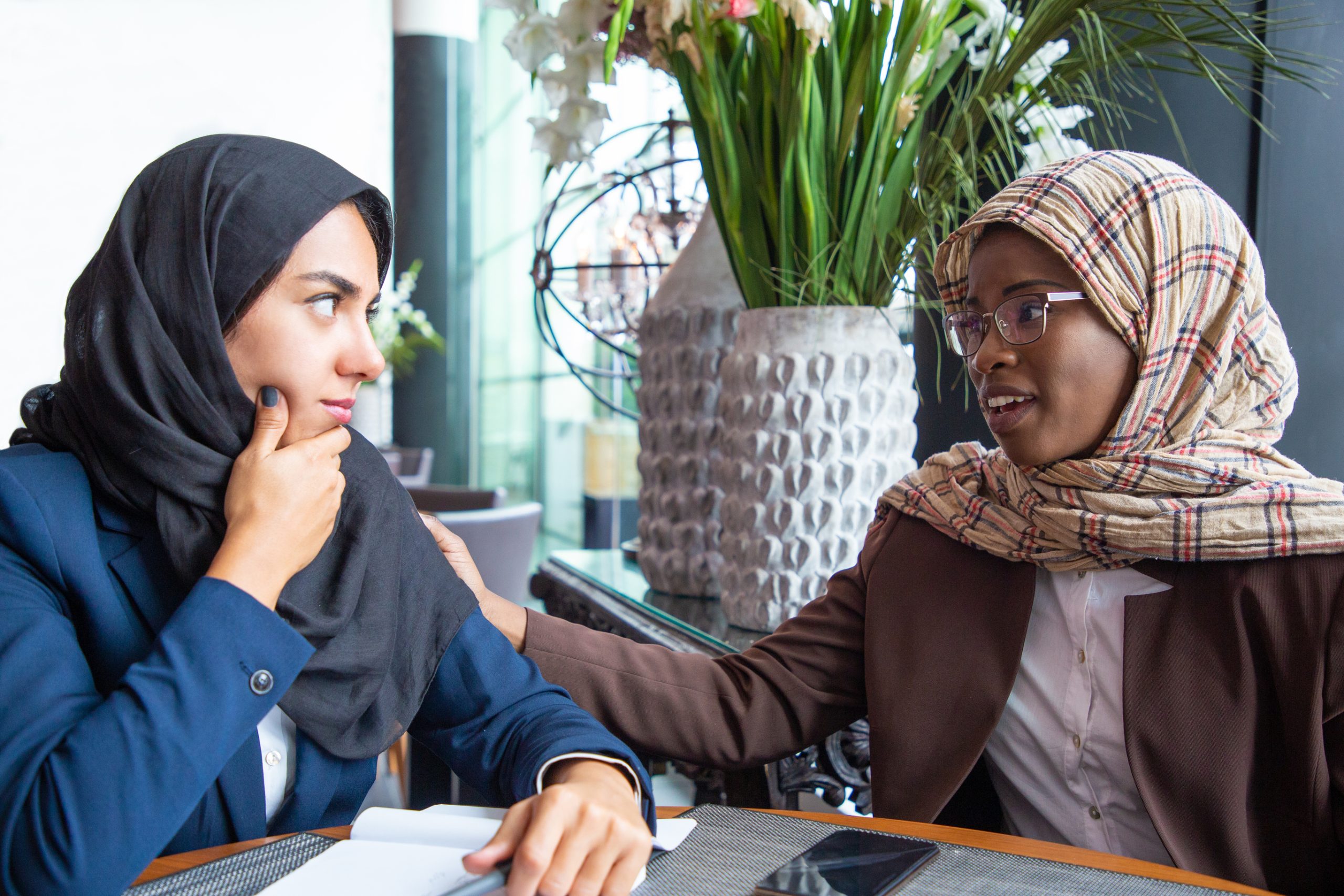 Two women in hijabs sitting at a desk having a serious conversation