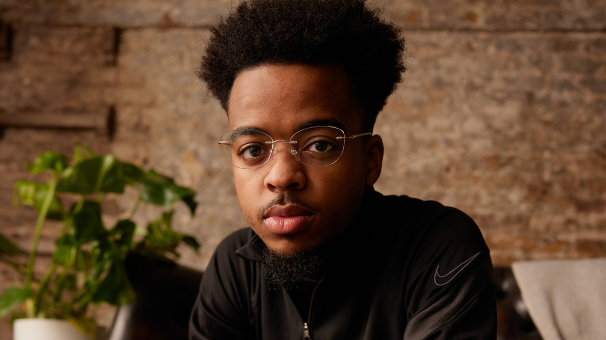 A young man in glasses sitting indoors, looking at the camera